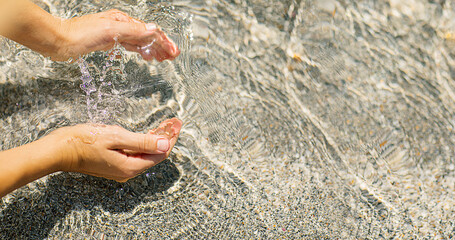 Close-up of woman's hands touching clean sea water with splash and sun glare during summer time....
