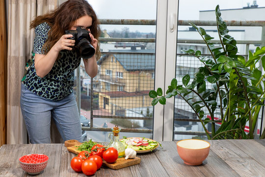 A food photographer taking a picture of arugula salad with cucumber and radish food on her digital camera. Young female photographer looking through camera lenses.
