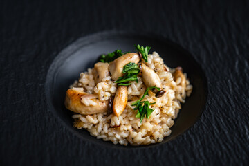Risotto mit Kräuterseitlingen Pilzen und Kräutern auf schwarzem Teller edel angerichtet