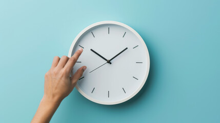 hand reaching out to a white wall clock on a light blue background, seemingly to adjust the time.