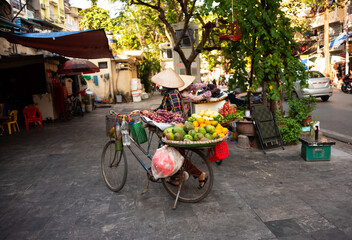 Fototapeta na wymiar Vietnam street vendors. Woman with traditional Vietnamese hat selling fruit from bicycle in Hanoi