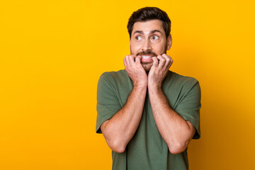 Photo of guilty scared man wear khaki t-shirt biting fingers looking empty space isolated yellow color background - obrazy, fototapety, plakaty