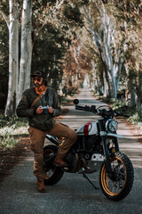 Fototapeta na wymiar Chico con barba con atuendo de motorista posando con su moto y su cámara 
