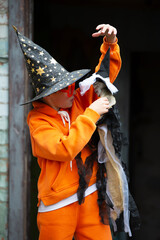 Fototapeta premium A child in an orange costume and a wizard hat for Halloween. A boy holds a skeleton at a Halloween party.