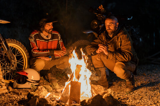 Pareja de amigos de noche junto a sus motos con una hoguera disfrutando de charla