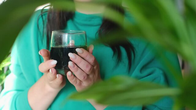 A woman holds a glass of chlorophyll, promoting body wellness. Start your day right with a blend of vitamins, minerals, and chlorophyll for a healthy morning routine.
