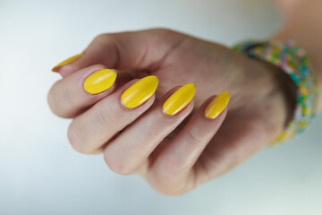 Female hand with long nails and a bottle of bright yellow orange nail polish	