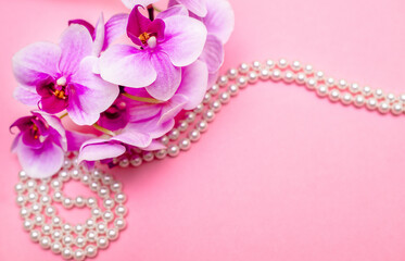 Pearl necklace and purple orchid on pink background