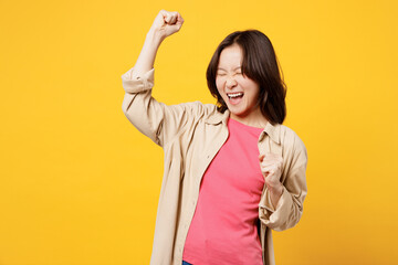 Young woman of Asian ethnicity wear pink t-shirt beige shirt pastel casual clothes doing winner gesture celebrate clench fists say yes isolated on plain yellow background studio. Lifestyle portrait.