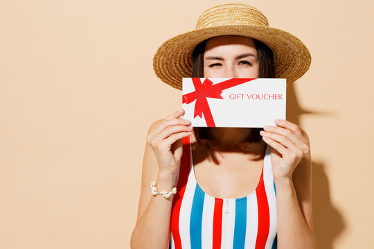 Young woman wear one-piece swimsuit straw hat near hotel pool hold cover mouth with gift certificate coupon voucher card for store isolated on plain beige background Summer sea rest sun tan concept.