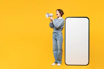 Fotobehang Full body young woman wears grey knitted sweater casual clothes big huge blank screen mobile cell phone smartphone with area scream in megaphone isolated on plain yellow background. Lifestyle concept. © ViDi Studio