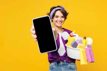 Young woman wears purple shirt hold basin with detergent bottles do housework tidy up hold use...