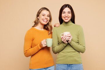 Young smiling fun friends two women they wear orange green shirt casual clothes together hold cup...