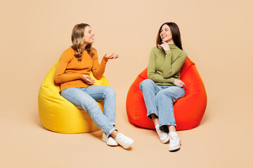 Full body young friends two women they wear orange green shirt casual clothes together sit in bag...