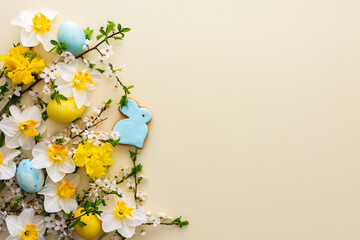 Festive background with spring flowers and naturally colored eggs and Easter bunnies, white daffodils and cherry blossom branches on a yellow pastel background
