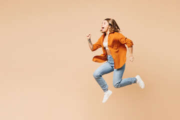 Fototapeta na wymiar Full body side profile view excited happy young woman wear orange shirt casual clothes jump high run fast hurry up isolated on plain pastel light beige background studio portrait. Lifestyle concept.