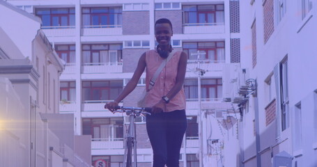 Image of light spots over happy african american woman walking with bicycle