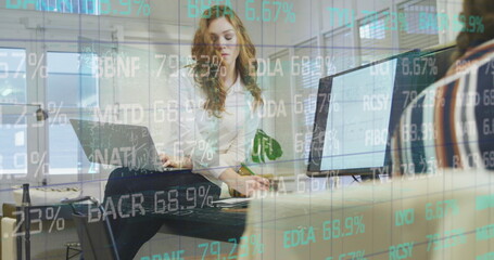 Image of financial data over caucasian businesswoman working on laptop in office