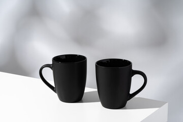 Two black ceramic mugs on gray background with shadows