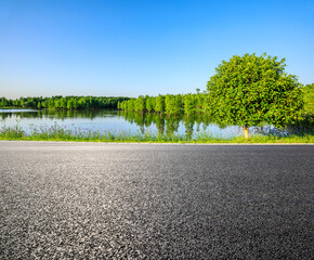 Asphalt road ground and lake with green forest nature landscape under blue sky