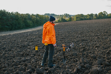 A young man searches for treasure with a metal detector in a plowed field.
