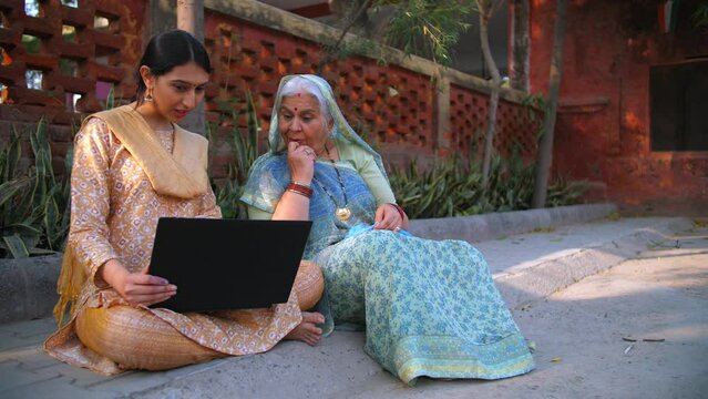 A beautiful young Indian using laptop with her grandma - dadi: success  happiness  topper girl. Old mother doing crochet feeling proud of her intelligent daughter - desi lifestyle  modern villagers...