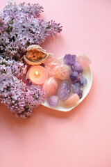 quartz minerals, candle, angel figurine and lilac flowers on pink background. gemstones for magic...