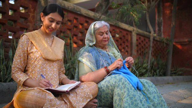 Beautiful young Indian girl studying - mother making sweater through crocheting  sincere girl  college going  village home  sitting on floor. Grey-haired old mother feeling proud of her studious da...