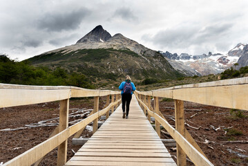 Fototapeta na wymiar woman contemplating and walking through beautiful landscape of mountains forests rivers and bridges lifestyle of traveling ushuaia argentina end of the world