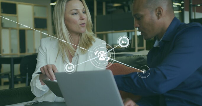Image of connected icons over diverse coworkers discussing reports on laptop in office - Powered by Adobe