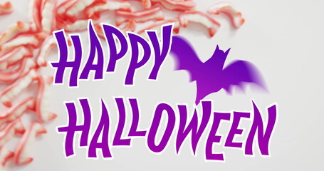 Happy halloween text banner with bat icon against halloween candies on grey surface