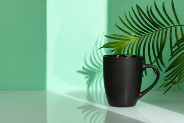 Porcelain mug and palm leaf against mint background