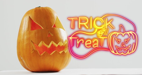 Obraz premium Neon trick or treat text banner with pumpkin icon over halloween pumpkins against grey background