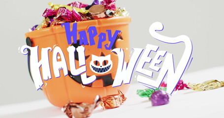 Image of happy halloween text with cat over orange pumpkin bucket with sweets