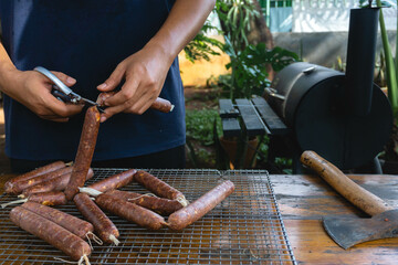 A man is cutting a sausage link that uses collagen casing, it will be cooked using the smoking technique