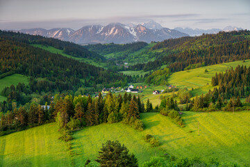 Spring view of the Tatra Mountains from Grandeus peak. Green meadow and trees in foreground. Tatra peaks partly covered by colorful clouds.
