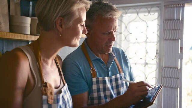 Mature Couple Working In Sustainable Plastic Free Grocery Store Checking Stock With Digital Tablet
