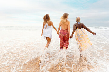 three young women holding hands walking towards the sea on a summer's day