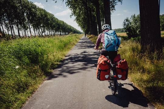 Frau radelt w&auml;hrend einer Radreise auf einem Radweg entlang eines Kanals in Flandern, Belgien