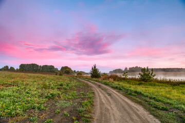 A rural landscape with a road extending into the distance. Dawn, early morning. Beautiful sky with bright red clouds.