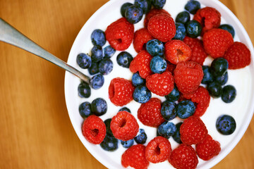 High angle, berries and nutrition with yogurt, raspberry and blueberry for organic snack. Food, cuisine and breakfast for health, wellness and diet for morning bowl or antioxidant wellbeing in studio