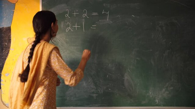 Indian teacher taking mathematics class of government school students - maths  blackboard teaching  green board. Beautiful teacher teaching basic level addition to students - sums  plus  minus  ele...