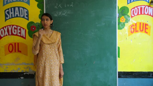 Female Indian teacher teaching basic multiplication to students - maths  mathematics class  blackboard teaching. Government school teacher asking for easy multiplication answers from students - tes...