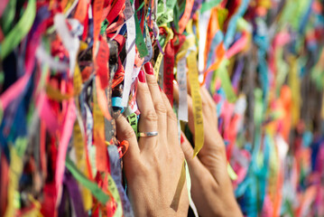 A person's hands are tying a souvenir ribbon on the railing of the Senhor do Bonfim church in the...