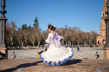 a little girl dancing flamenco dressed in a beige dress with ruffles and purple fringes in a famous...