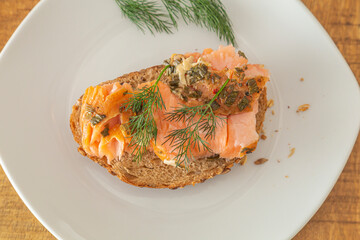 A piece of fresh bread with smoked salmon and a sprig of dill. High angle view. Closeup.
