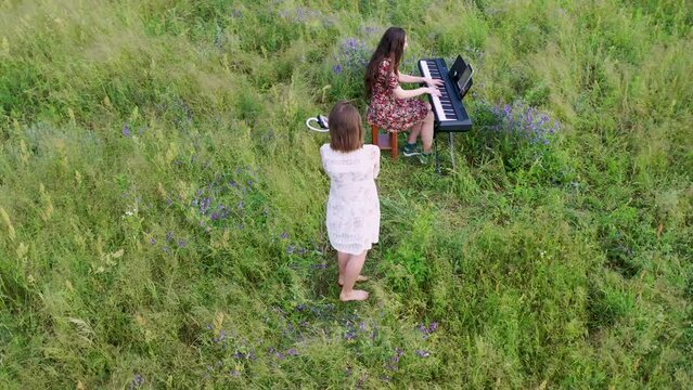Two young women musicians play piano and tune in a green field in summer. The video was shot in general plan in 4K aerial