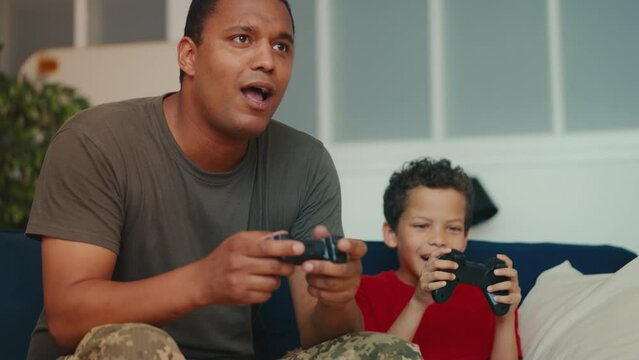 An African American soldier enjoys playing a video game with his young son