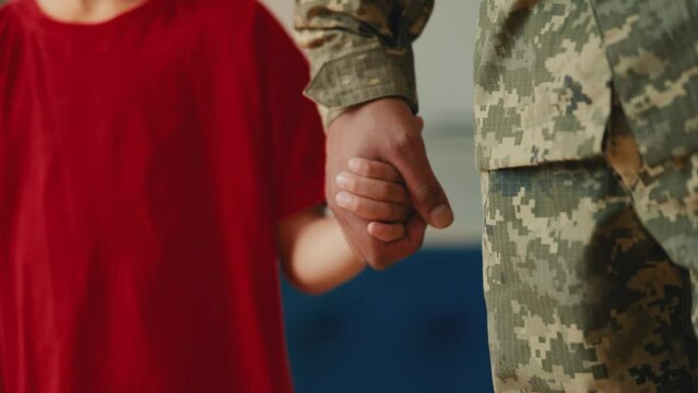A boy holds his soldier father's hand, parent leaving for military service