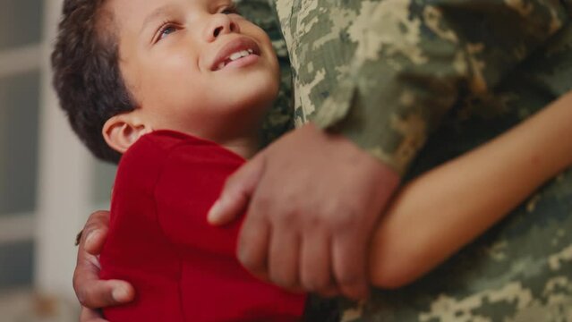 A happy boy wraps his arms around dad in military uniform, greeting his comeback